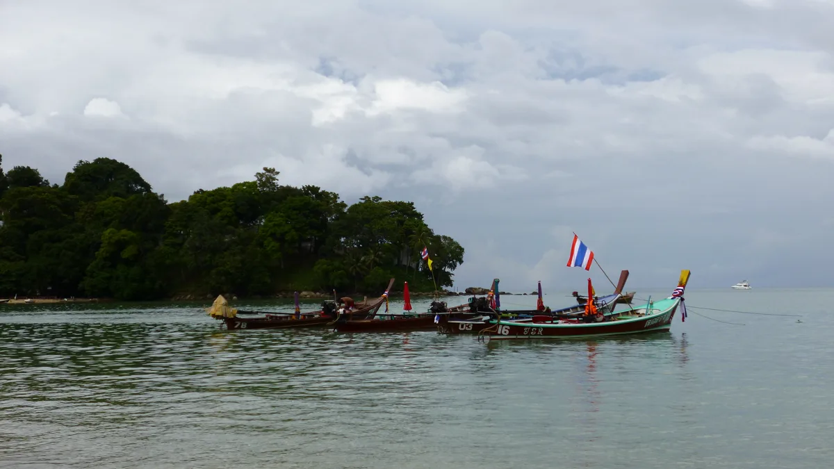 Long-tail boats resting off Patong Beach under a cloudy sky